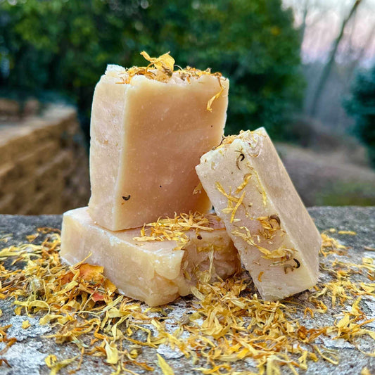 Three bars of soap with dried flowers on a stone surface outdoors