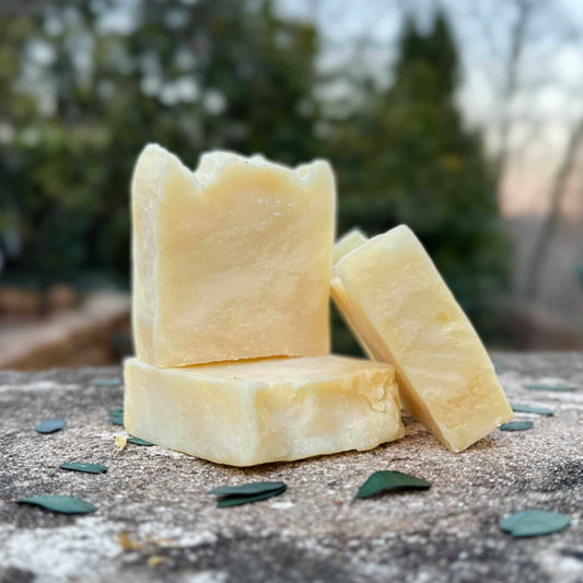 Three bars of soap stacked on a textured surface with a blurred natural background