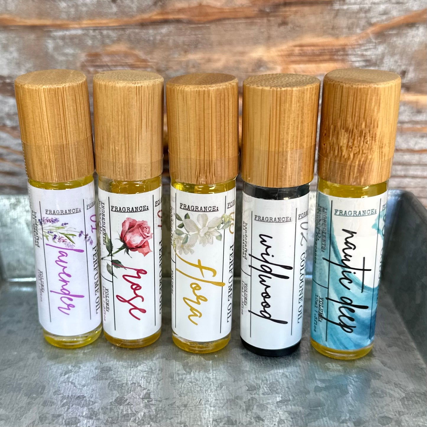 Five rollerball bottles of signature perfume and cologne with bamboo caps on a rustic surface.