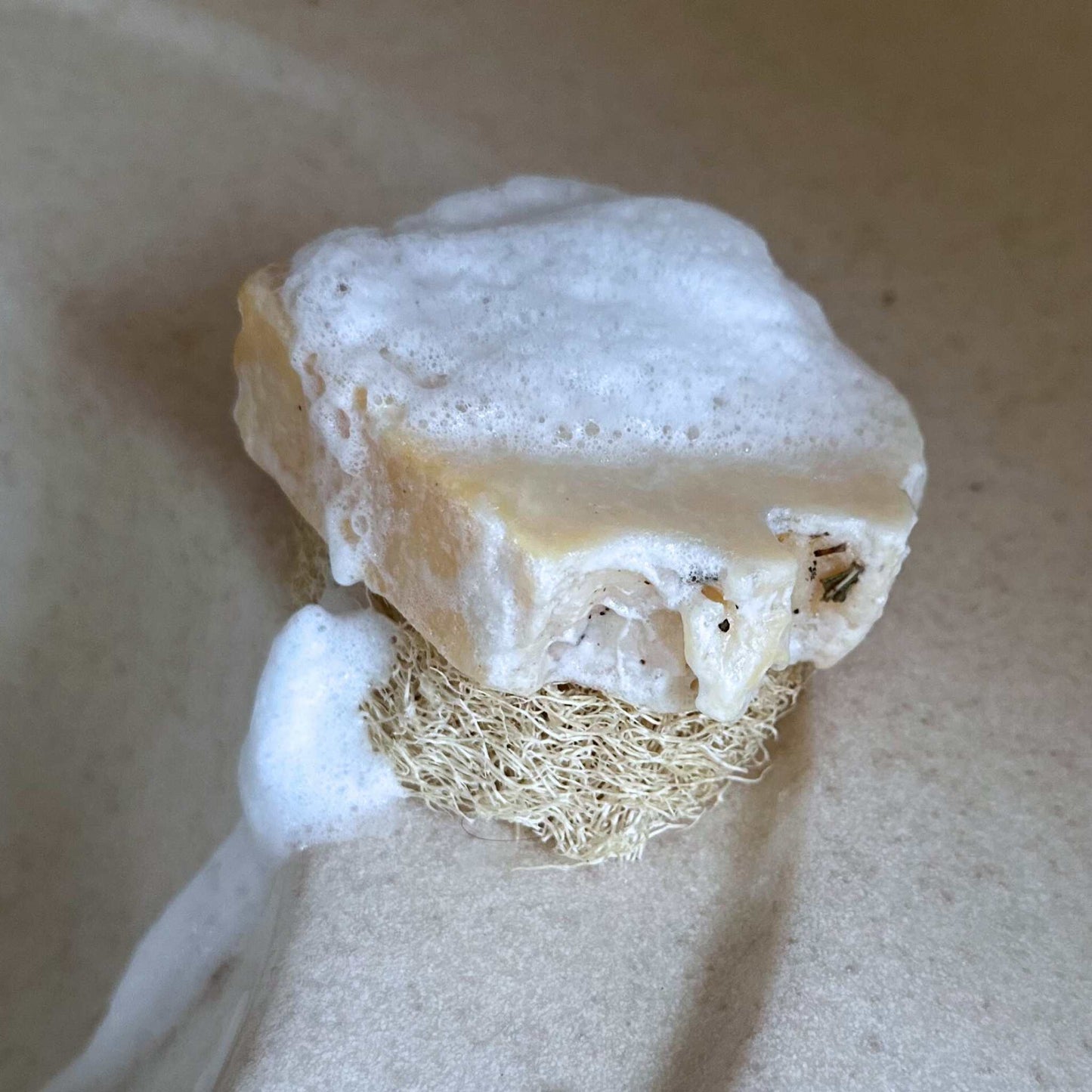 Foamy bar of soap with a loofah on a beige background