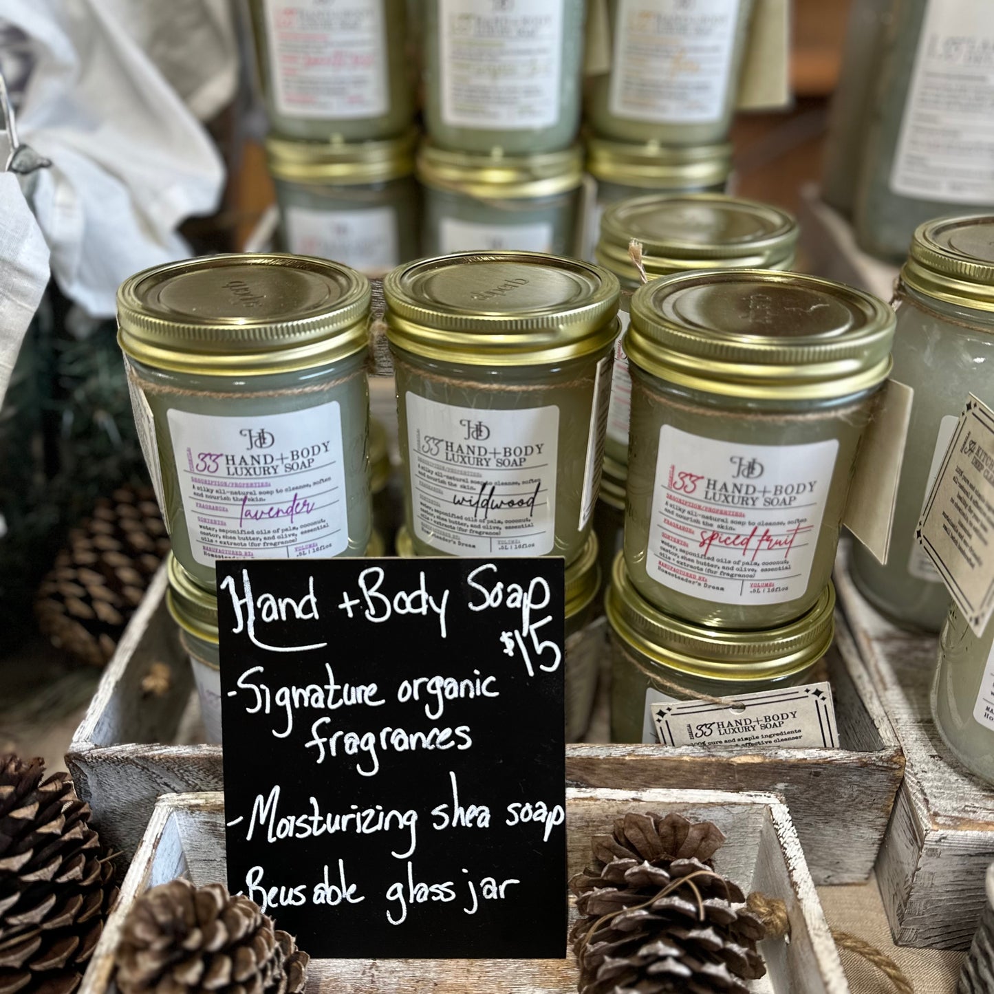 our all natural luxurious hand and body liquid soaps in a variety of scents, stacked in wooden crates with pinecone decor