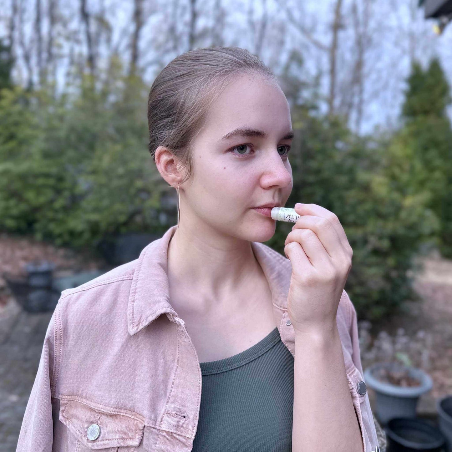 Person applying lip balm outdoors with trees in the background