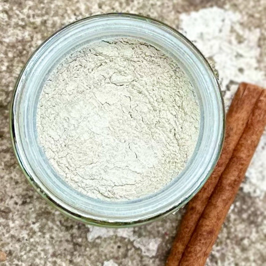 Jar of cinnamon toothpaste powder with cinnamon sticks on a textured surface