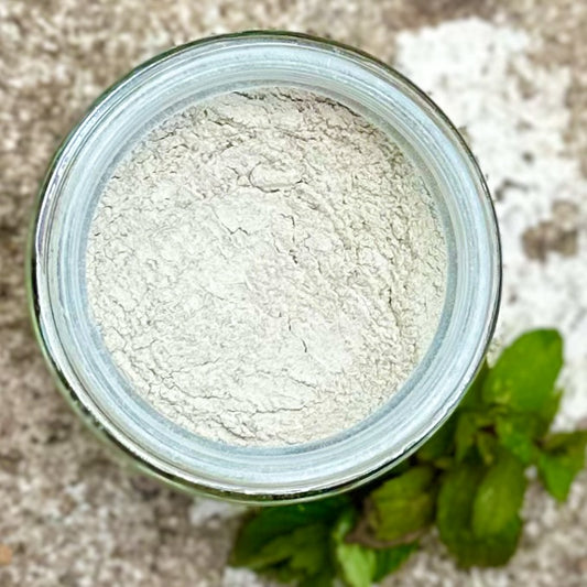 Jar of peppermint toothpaste powder with mint leaves on a textured surface