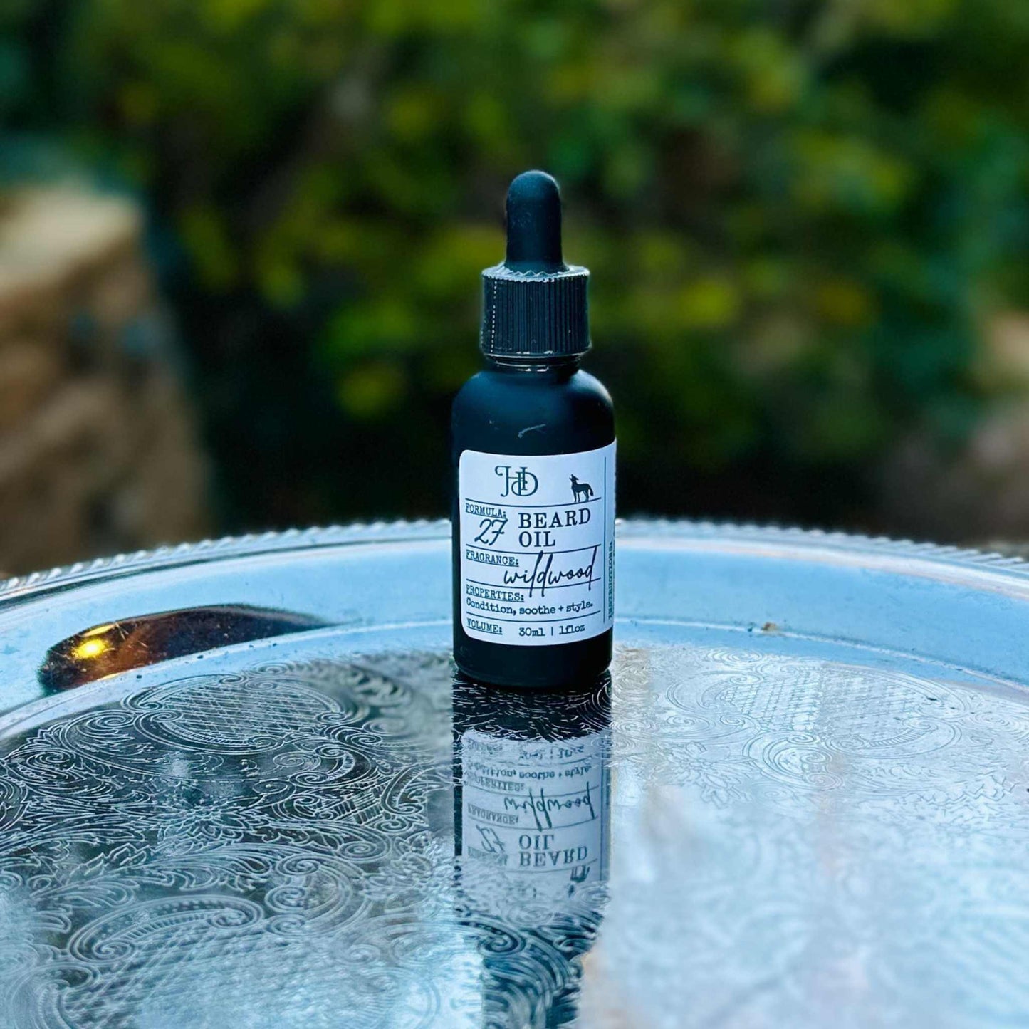 Bottle of beard oil on a reflective surface with a blurred natural background