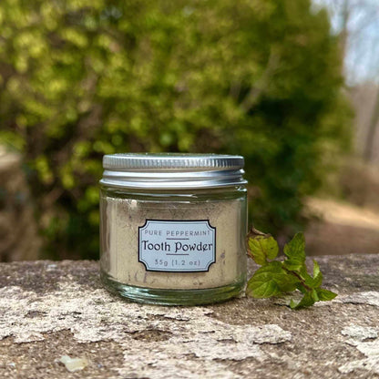 Jar of tooth powder with a label on a natural stone surface with greenery in the background