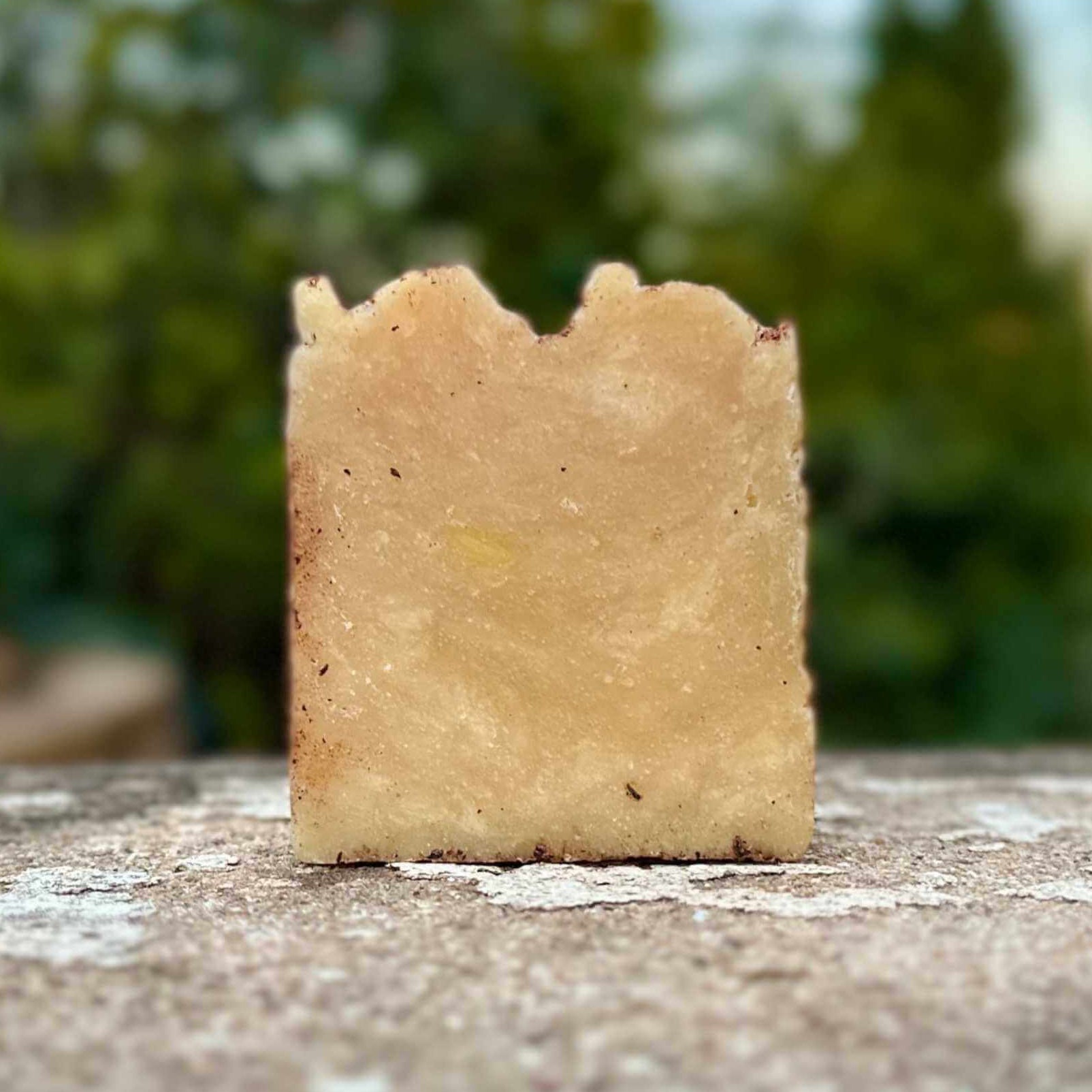 Square bar of soap on a textured surface with a blurred natural background
