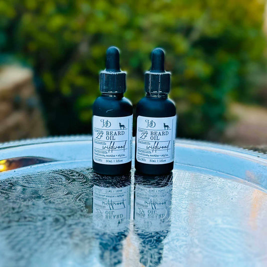 Two bottles of beard oil on a reflective surface with a blurred natural background