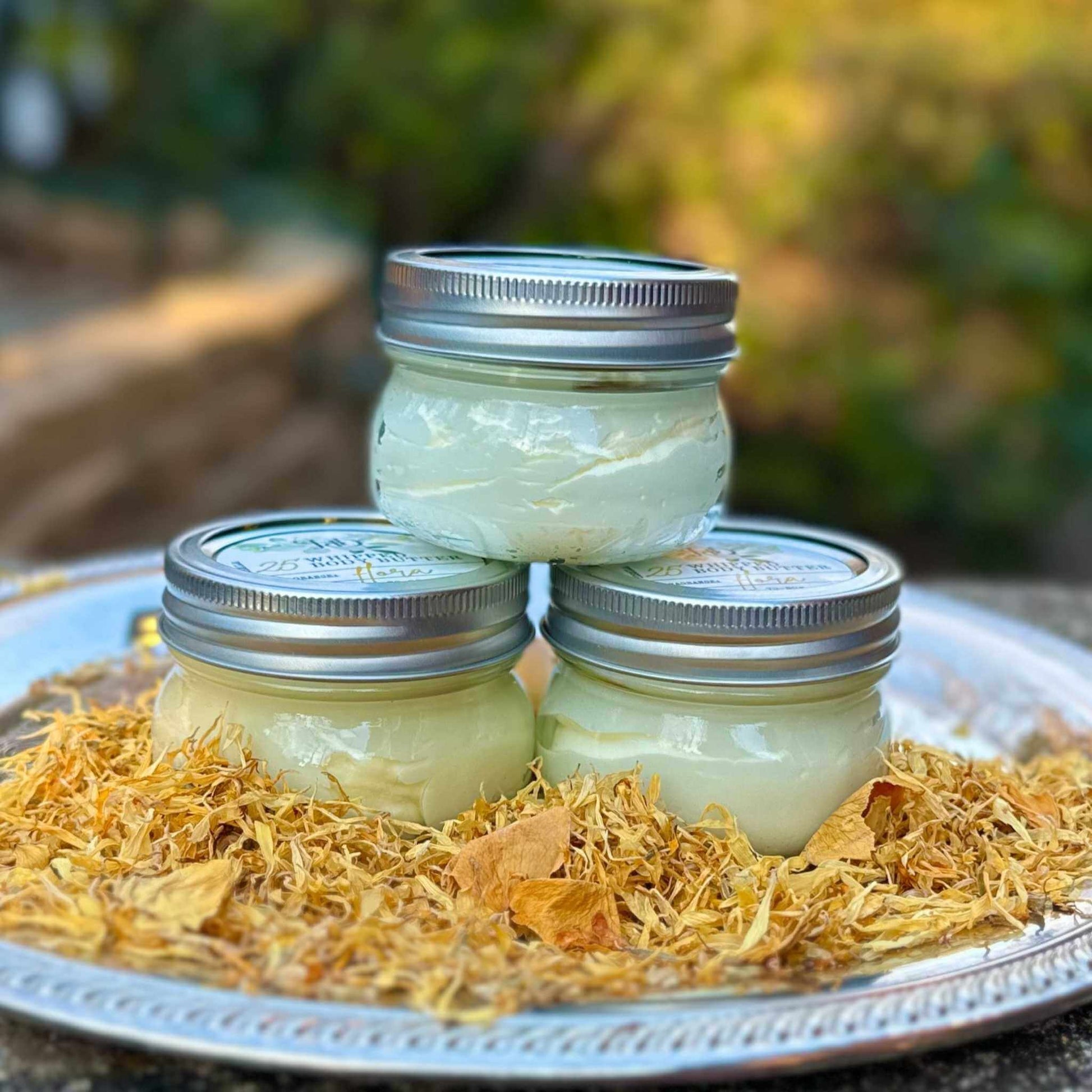 Three jars of cream stacked on a metal tray with a natural background