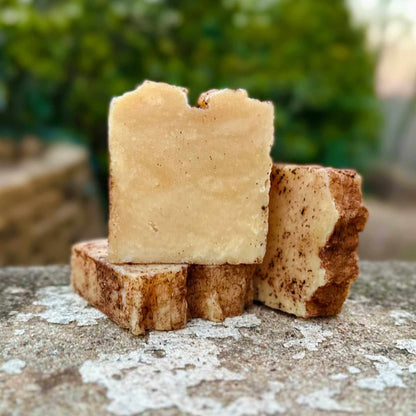 Three pieces of shea soap stacked on a textured surface with a blurred green background