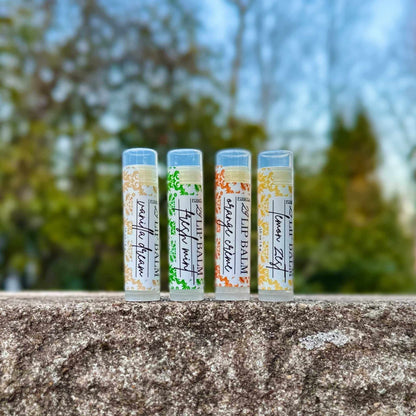 Four lip balm tubes with labels on a stone ledge outdoors.