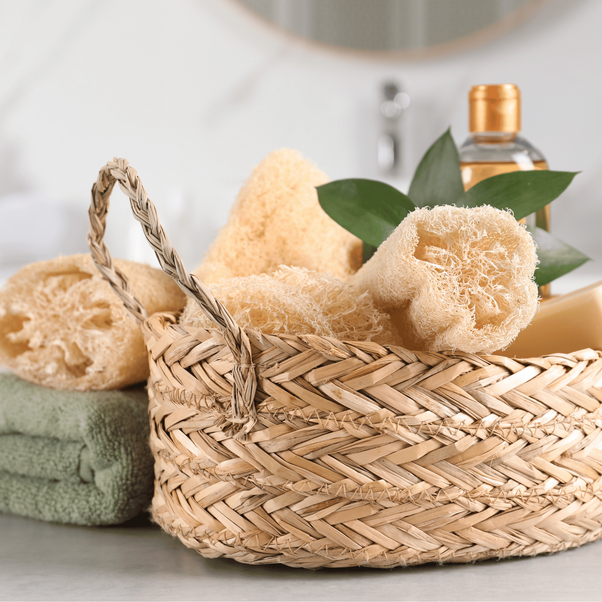 Wicker basket with loofahs, a towel, and soap on a bathroom counter.