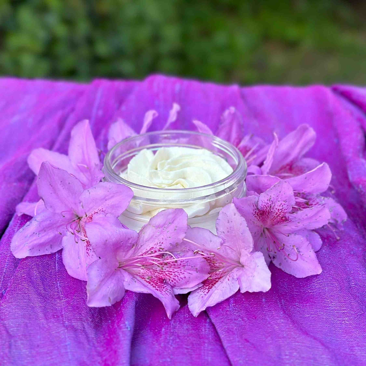lavender body butter surrounded by lavender azaleas on purple satin