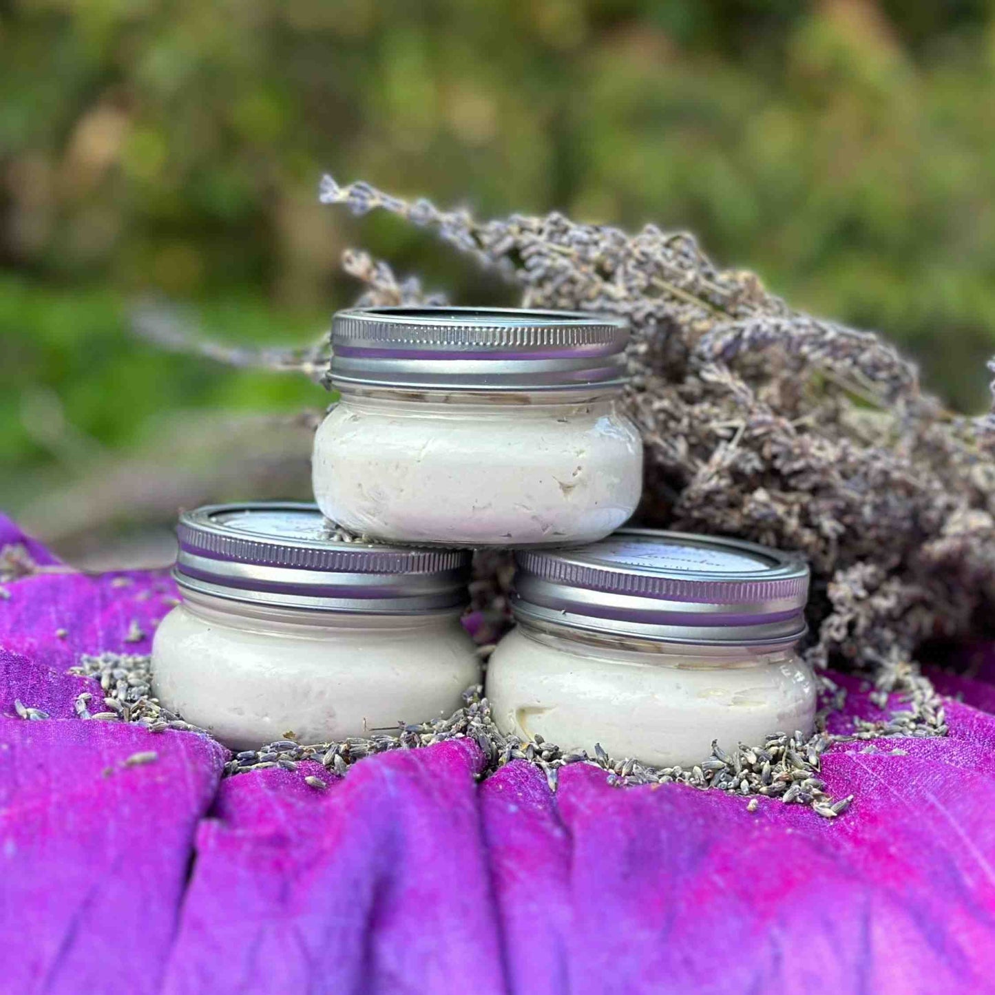 stack of 3 lavender body butter jars with a lavender bouquet on purple satin