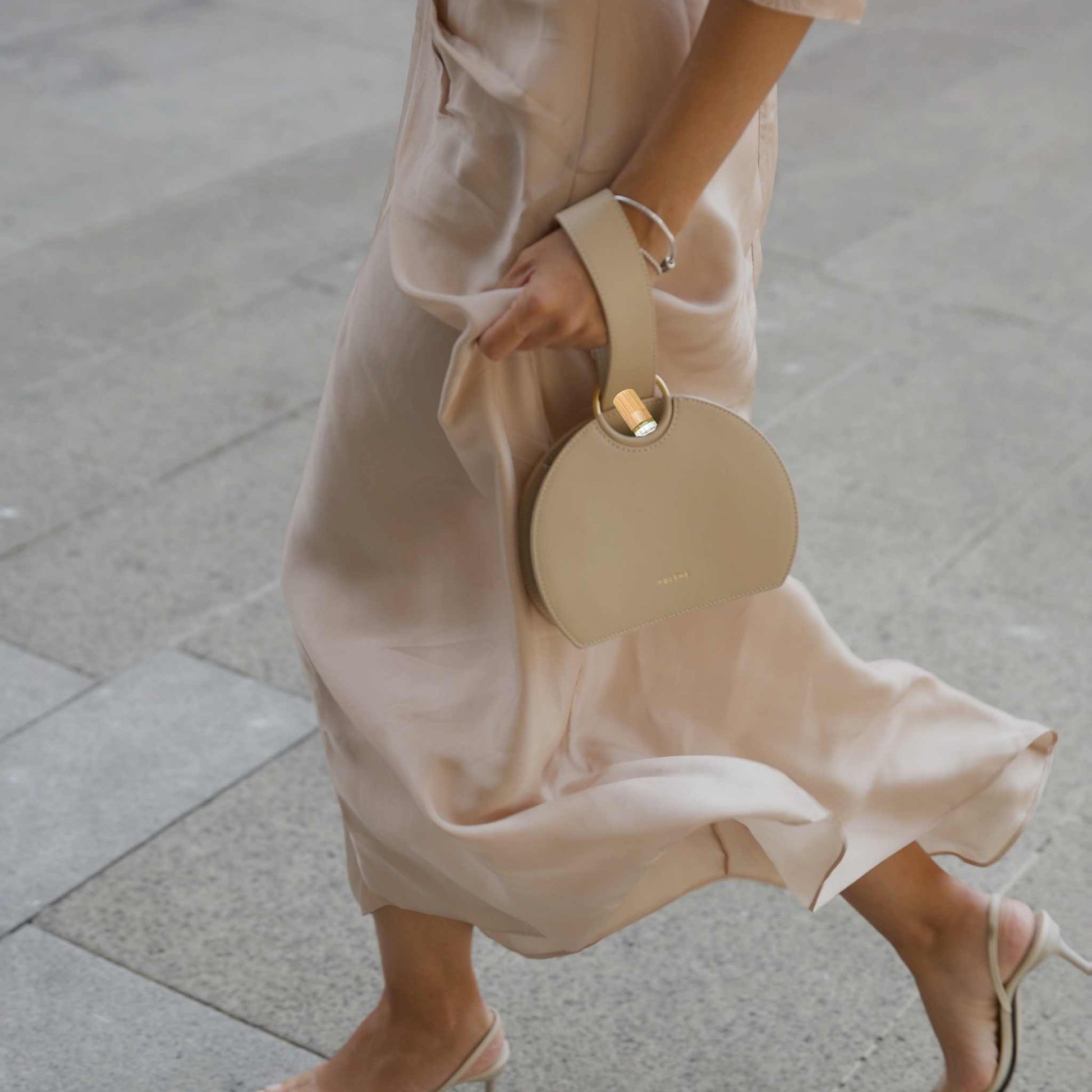 Woman holding a beige handbag on a sidewalk