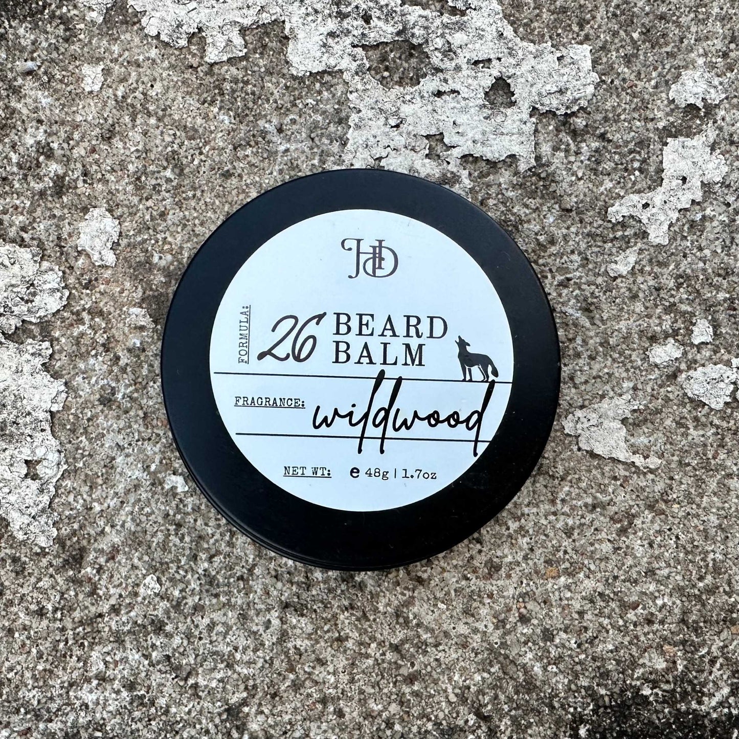 Beard balm tin with 'wildwood' fragrance on a textured surface
