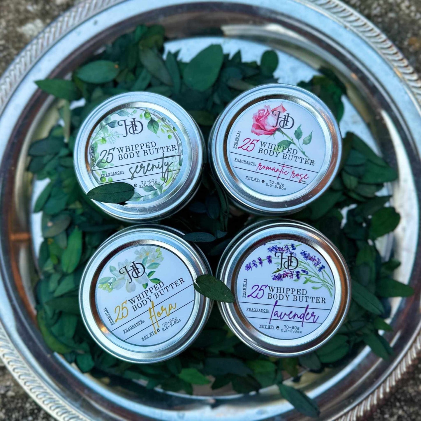 Four jars of 'Whipped Body Butter' on a decorative tray with green leaves