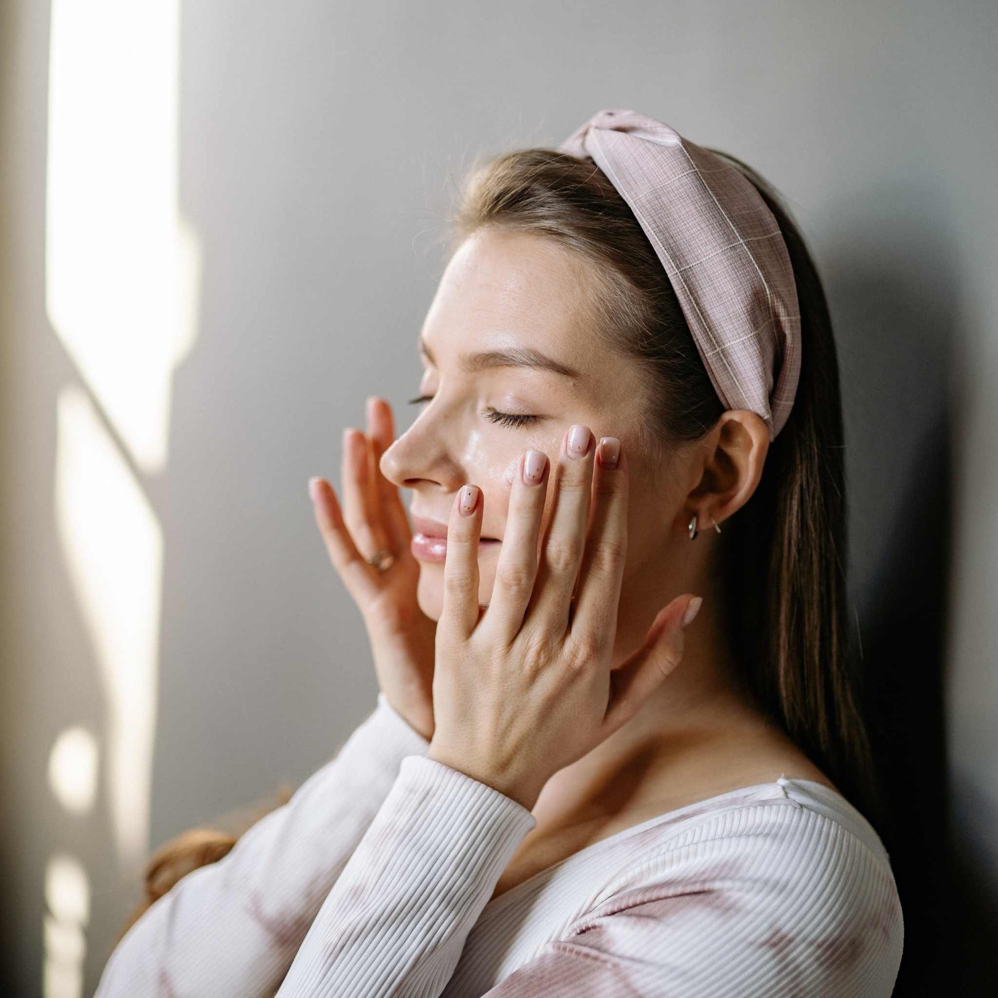 Woman with a pink headband touching her face in a softly lit room
