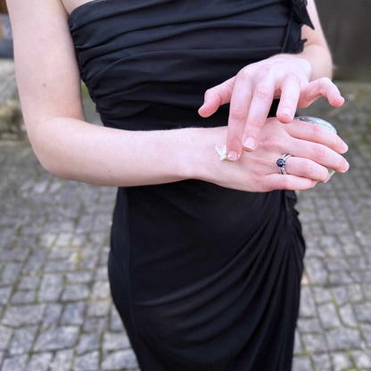 Person wearing a black dress with a blurred background applying body butter to hands