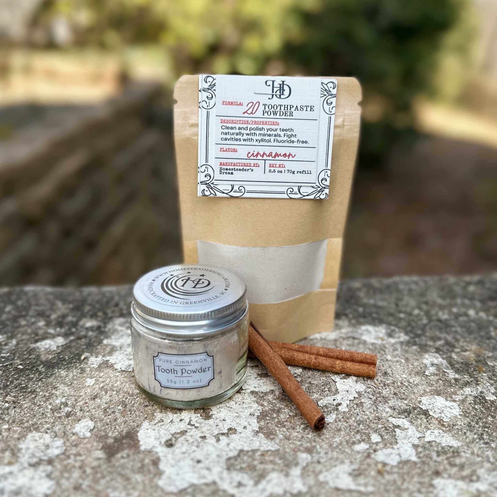 Jar of tooth powder and refill on a stone surface with cinnamon sticks.