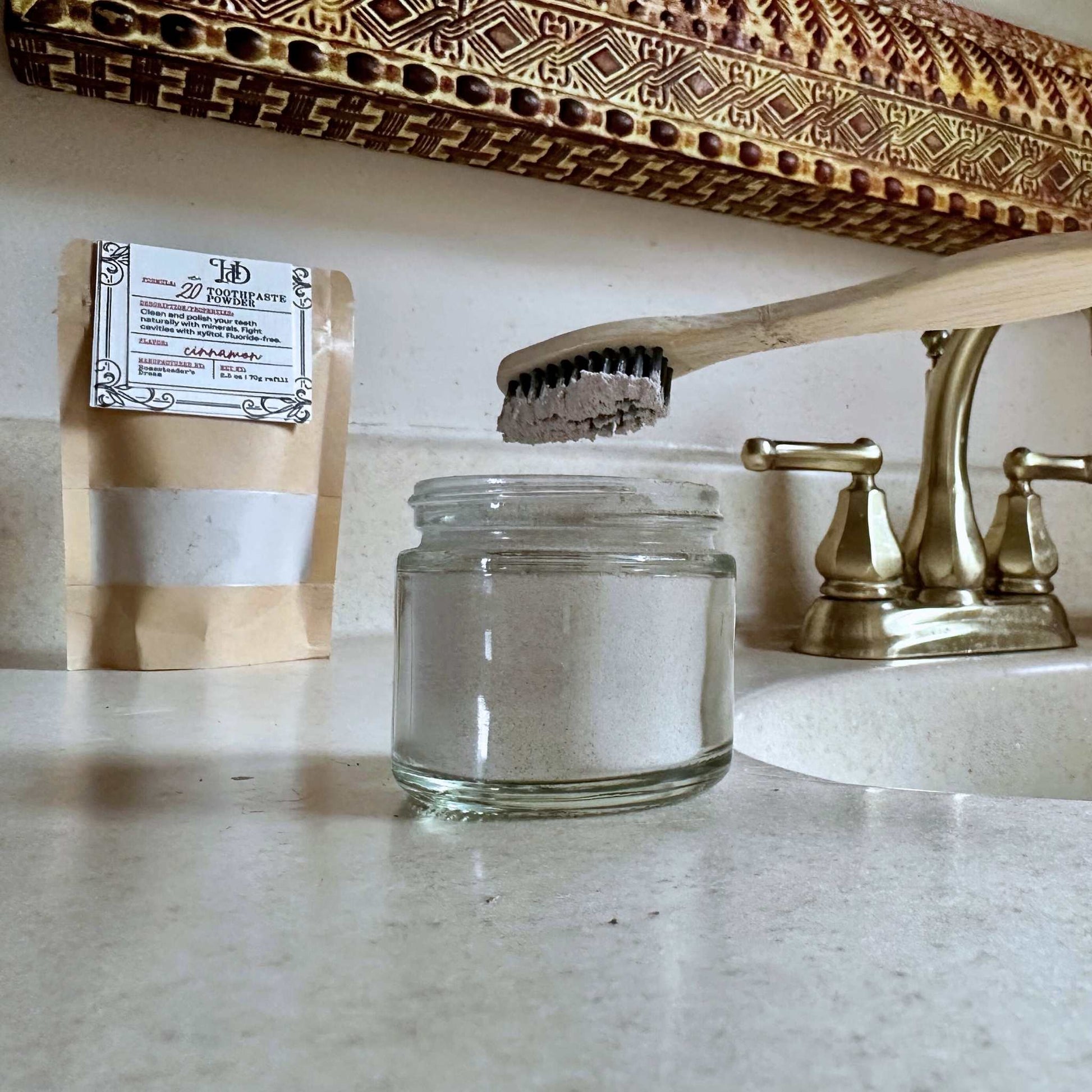 Clear glass jar on a bathroom counter with a wooden toothbrush and brown Kraft refill bag.