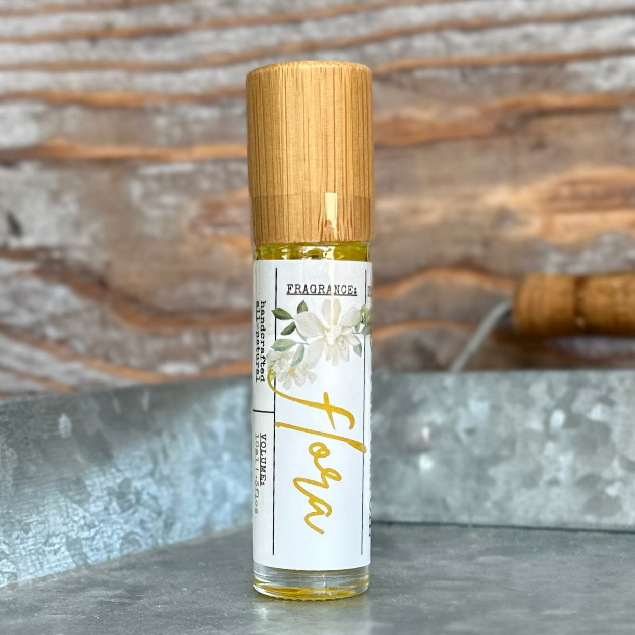 Roll-on glass bottle with bamboo lid on a metal tray with a rustic background