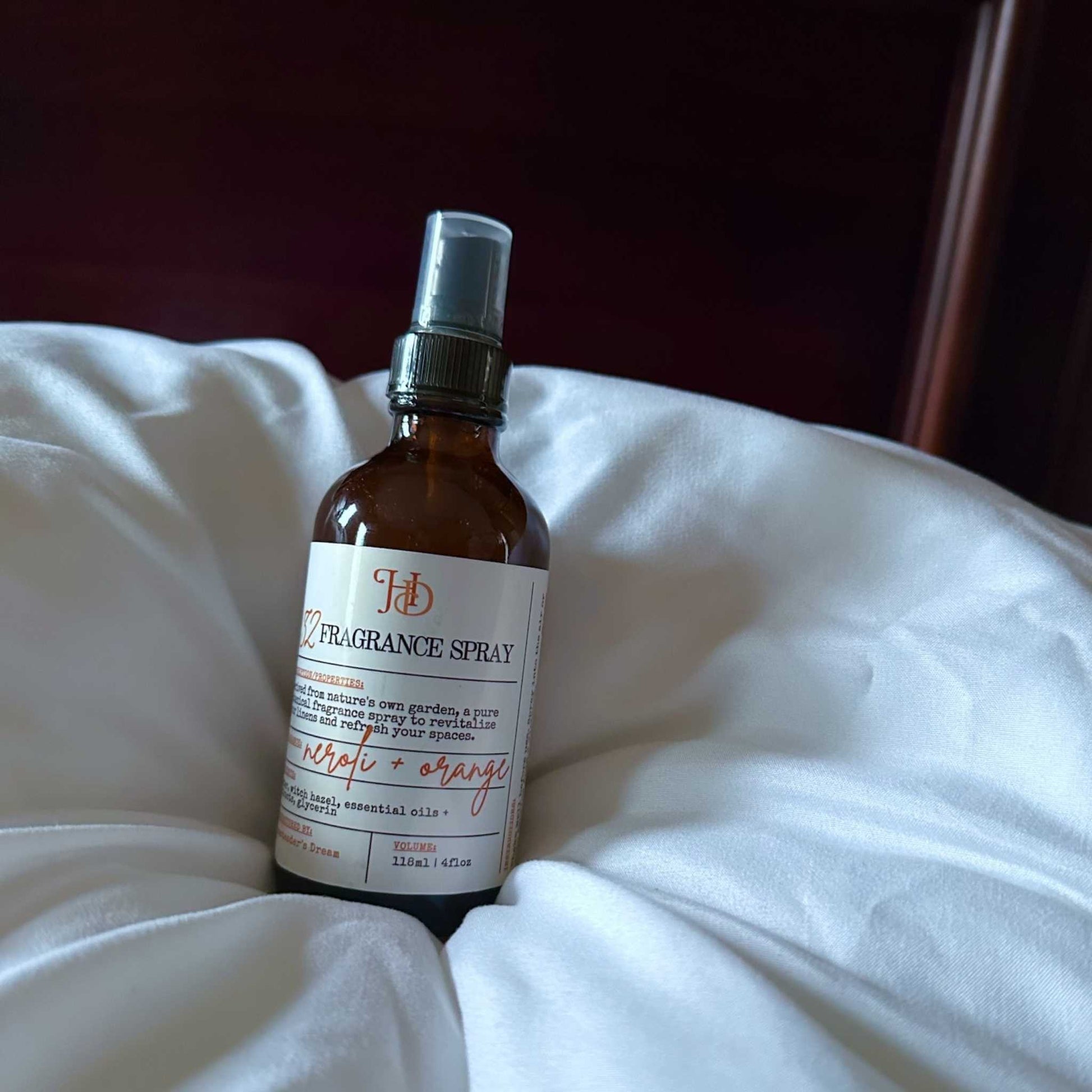 Fragrance spray bottle labeled 'HD' on white linens 