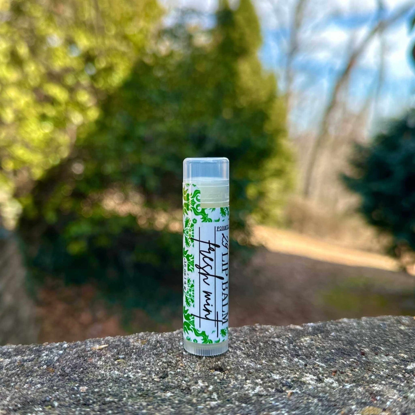 Lip balm tube with green label on a stone surface with blurred natural background