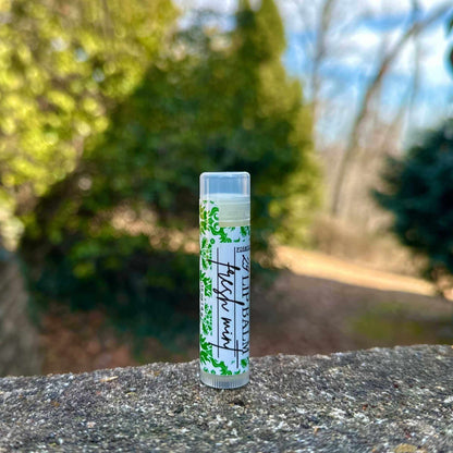 Lip balm tube with green label on a stone surface with blurred natural background