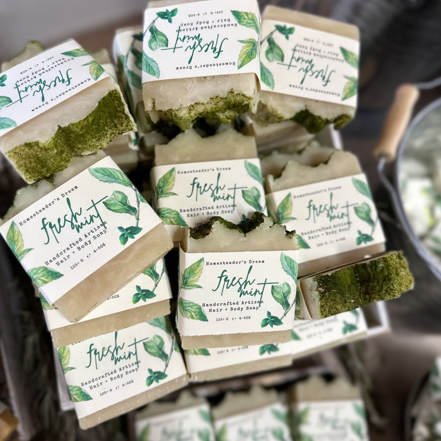 Stacks of artisan soap bars with 'Fresh Mint' labels on a wooden surface.