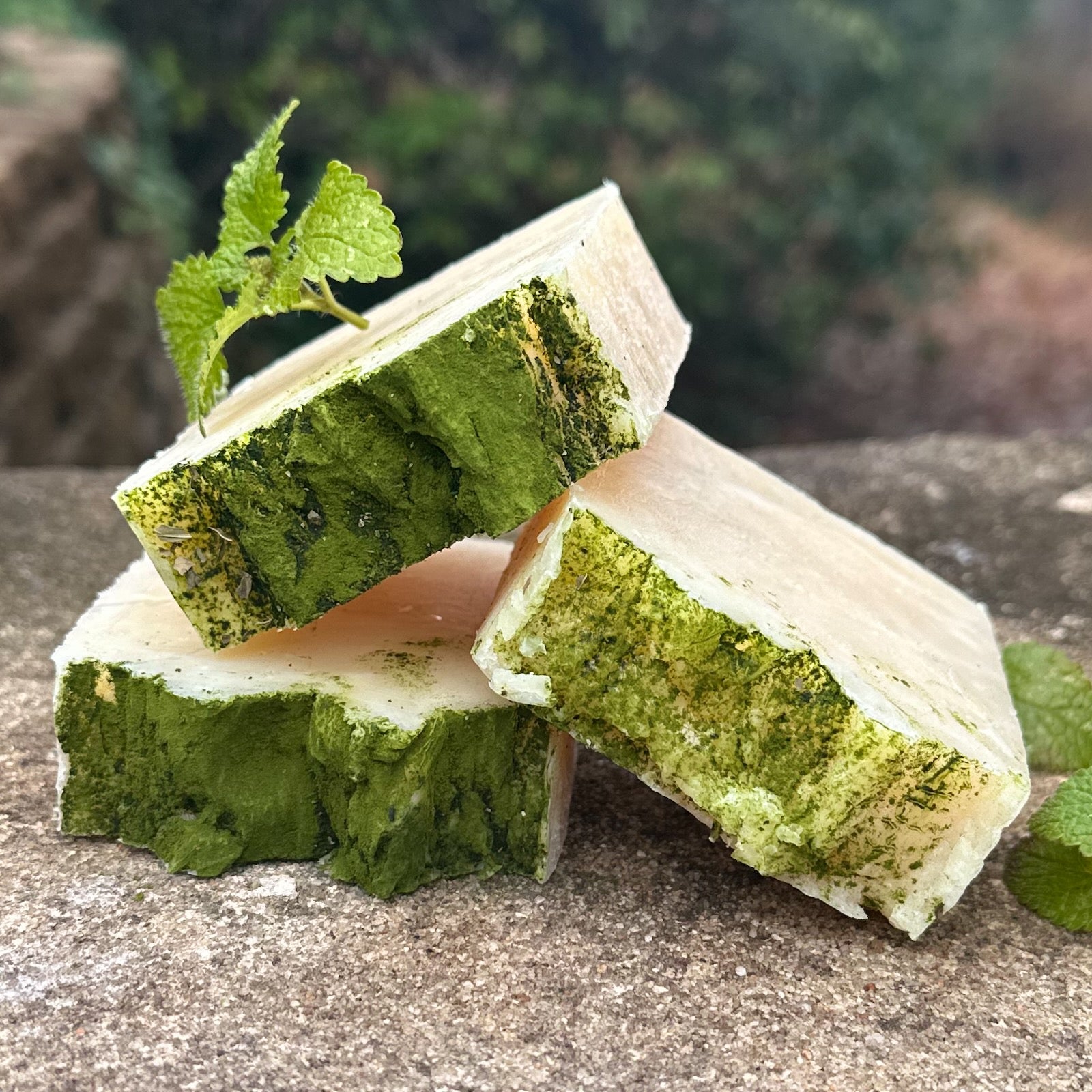 Green and white layered soap bars with a leaf on a stone surface