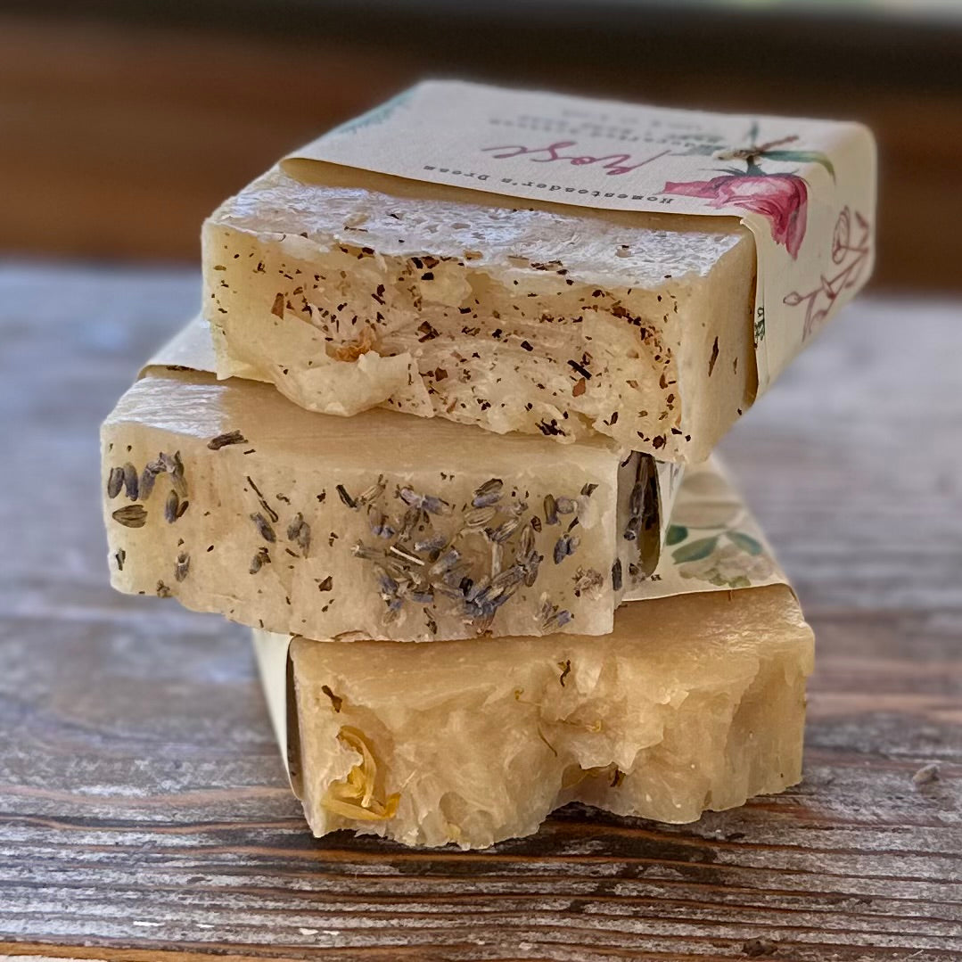 Stack of natural soap bars with visible herbs on a wooden surface