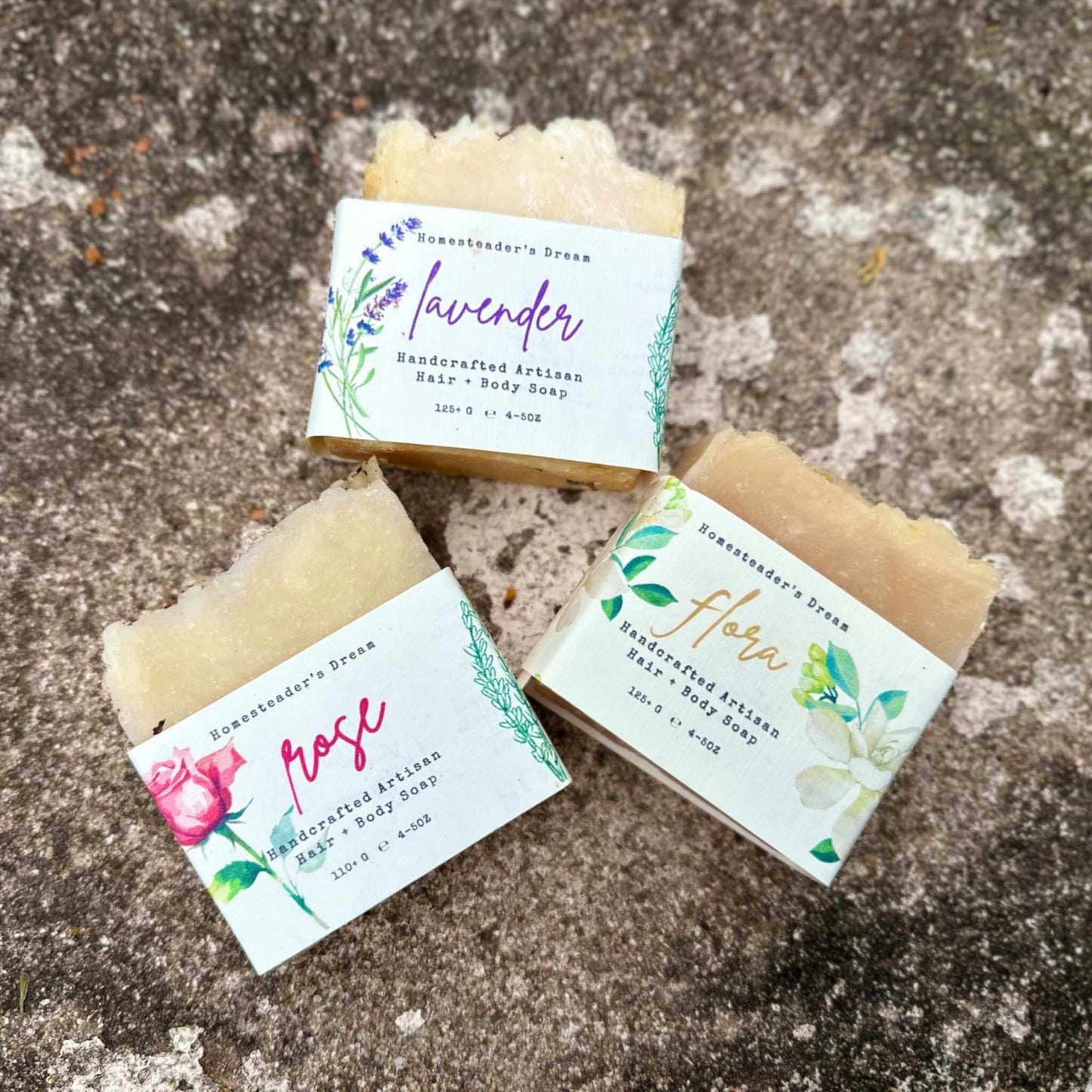 Three bars of floral soap with linen labels on a stone surface