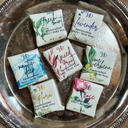 Assorted handcrafted hair and body guest soaps with designer labels on a silver tray.