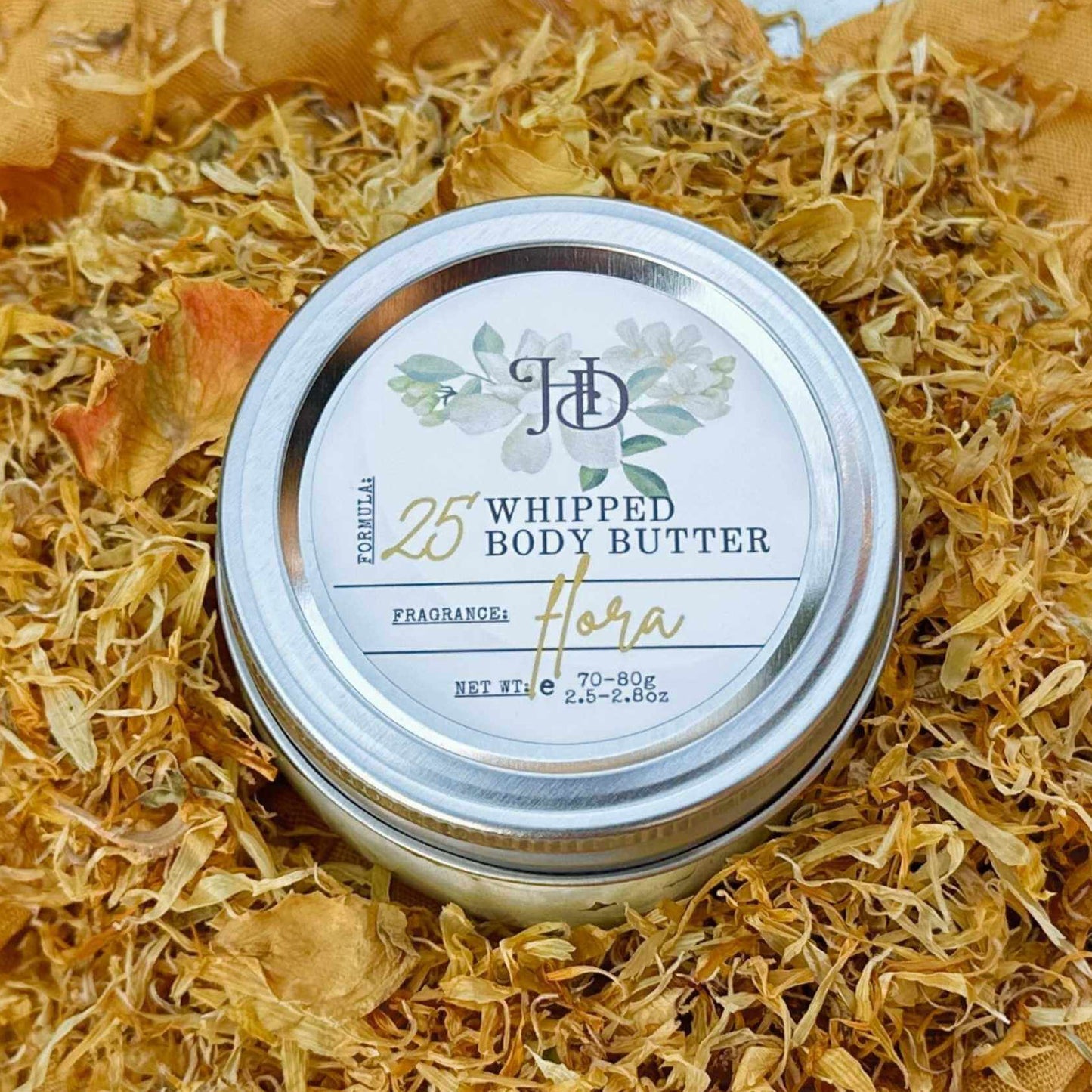 Jar of whipped body butter with a decorative lid on a bed of dried flowers.