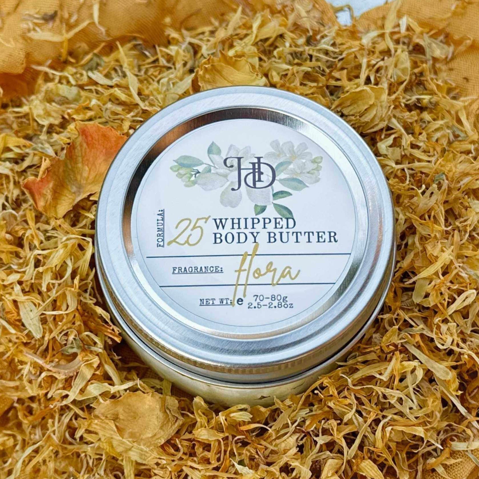 Jar of whipped body butter with a decorative lid on a bed of dried flowers.