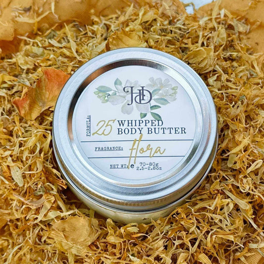 Jar of whipped body butter with a decorative lid on a bed of dried flowers.