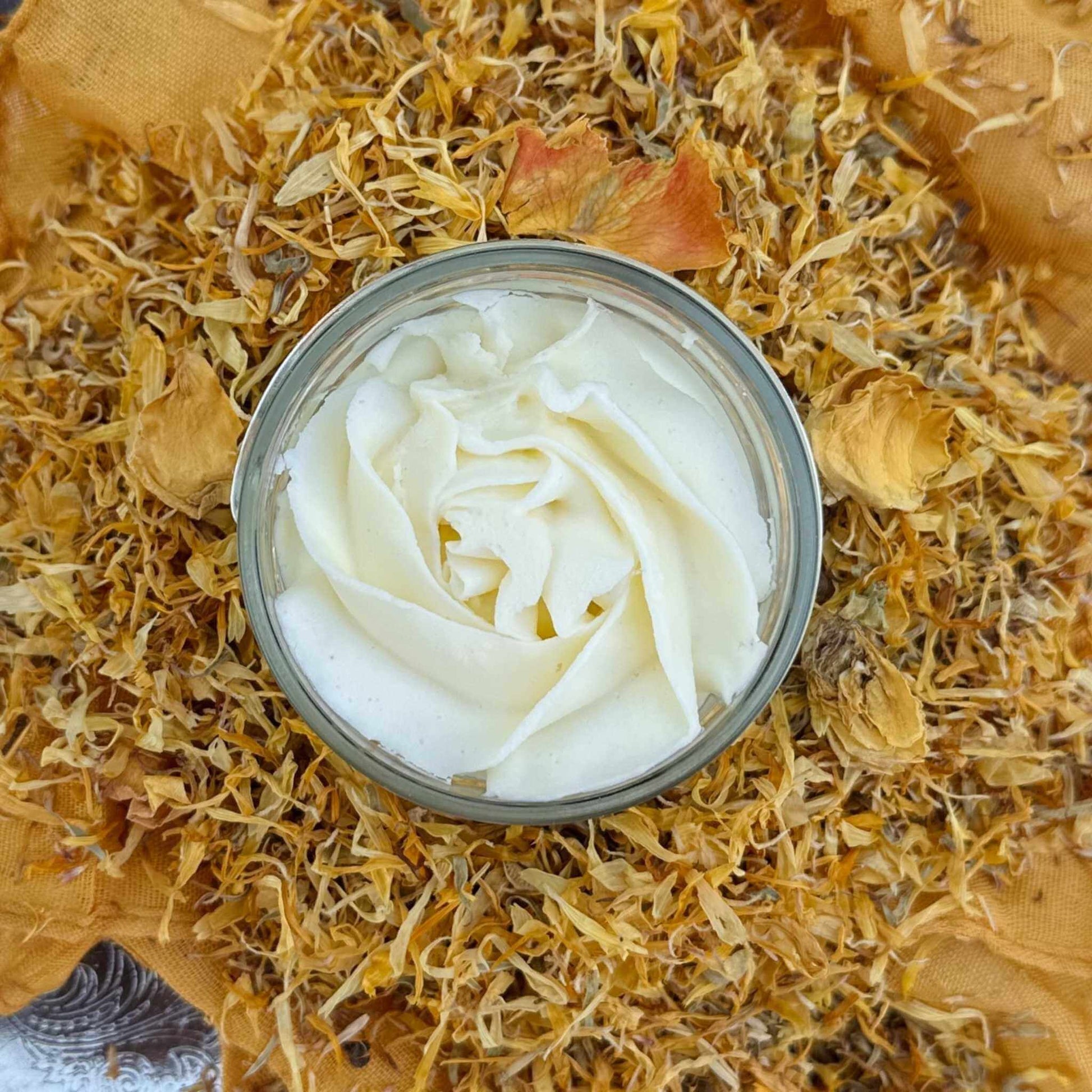 Jar of white jasmine body butter surrounded by dried flowers and leaves
