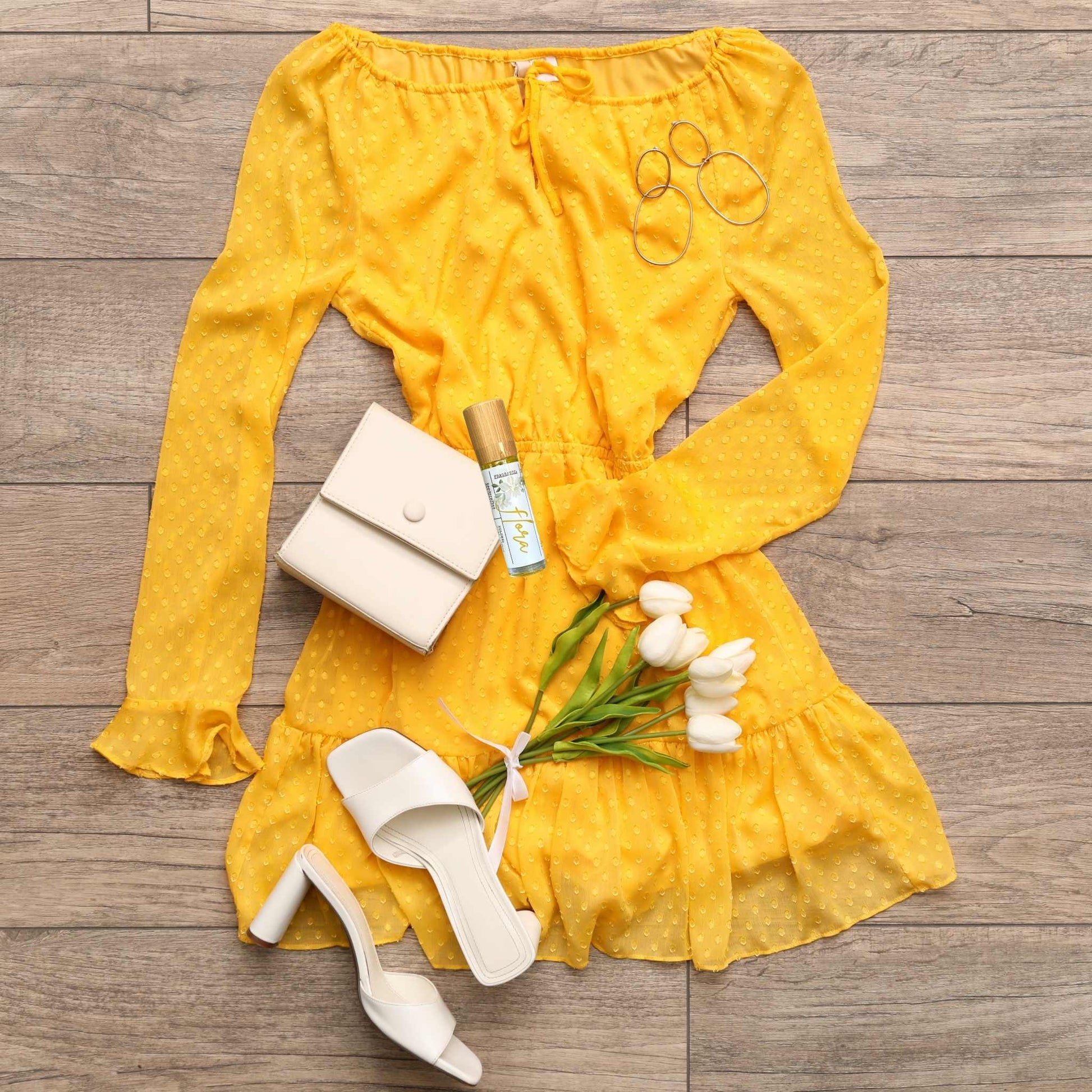 Yellow dress with white shoes, handbag, and flowers on a wooden surface