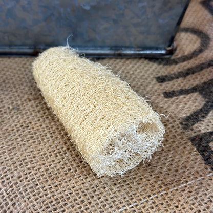 A natural beige loofah sponge on a textured background.