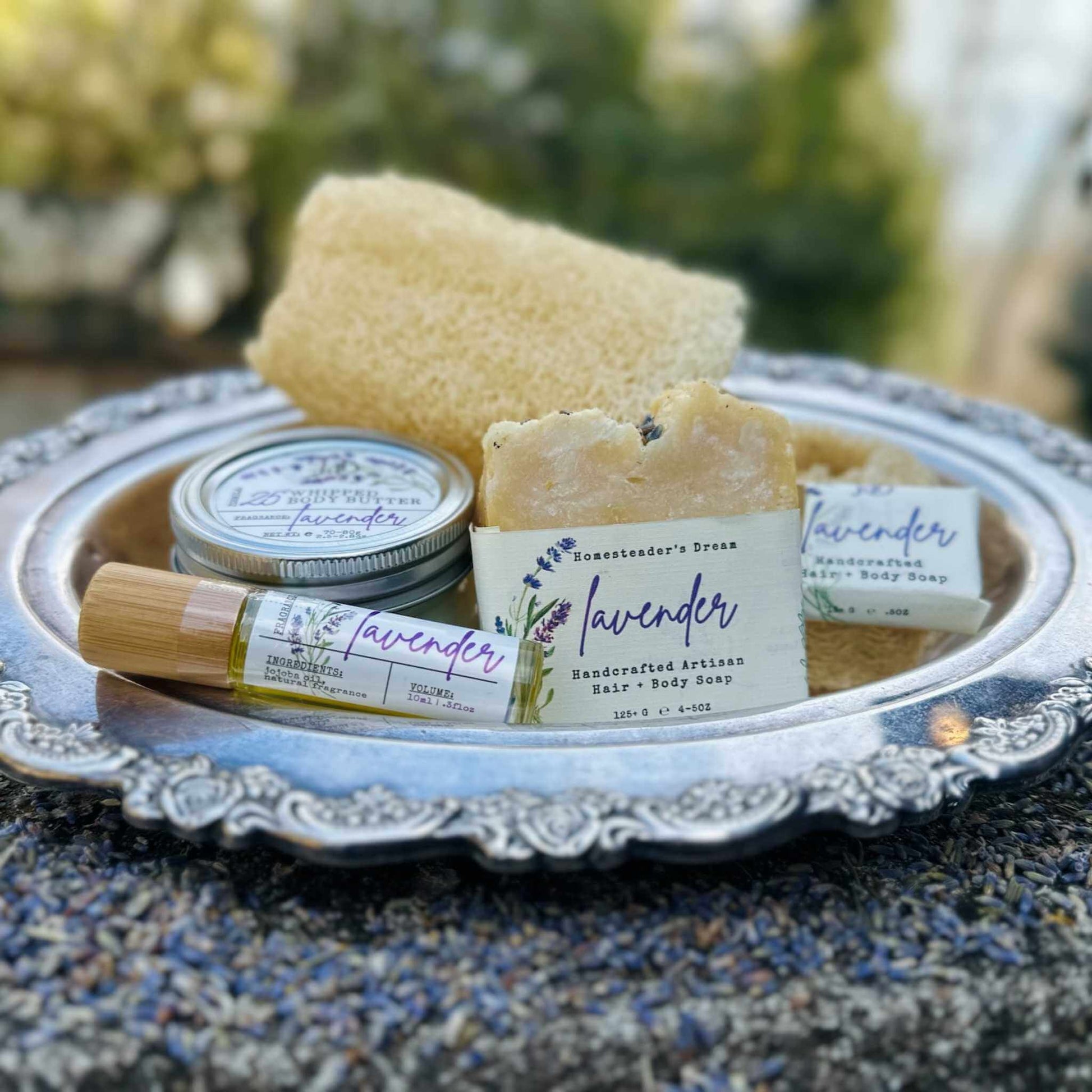 Lavender-themed products including soap, body wash, and loofah on a decorative tray with a blurred natural background.