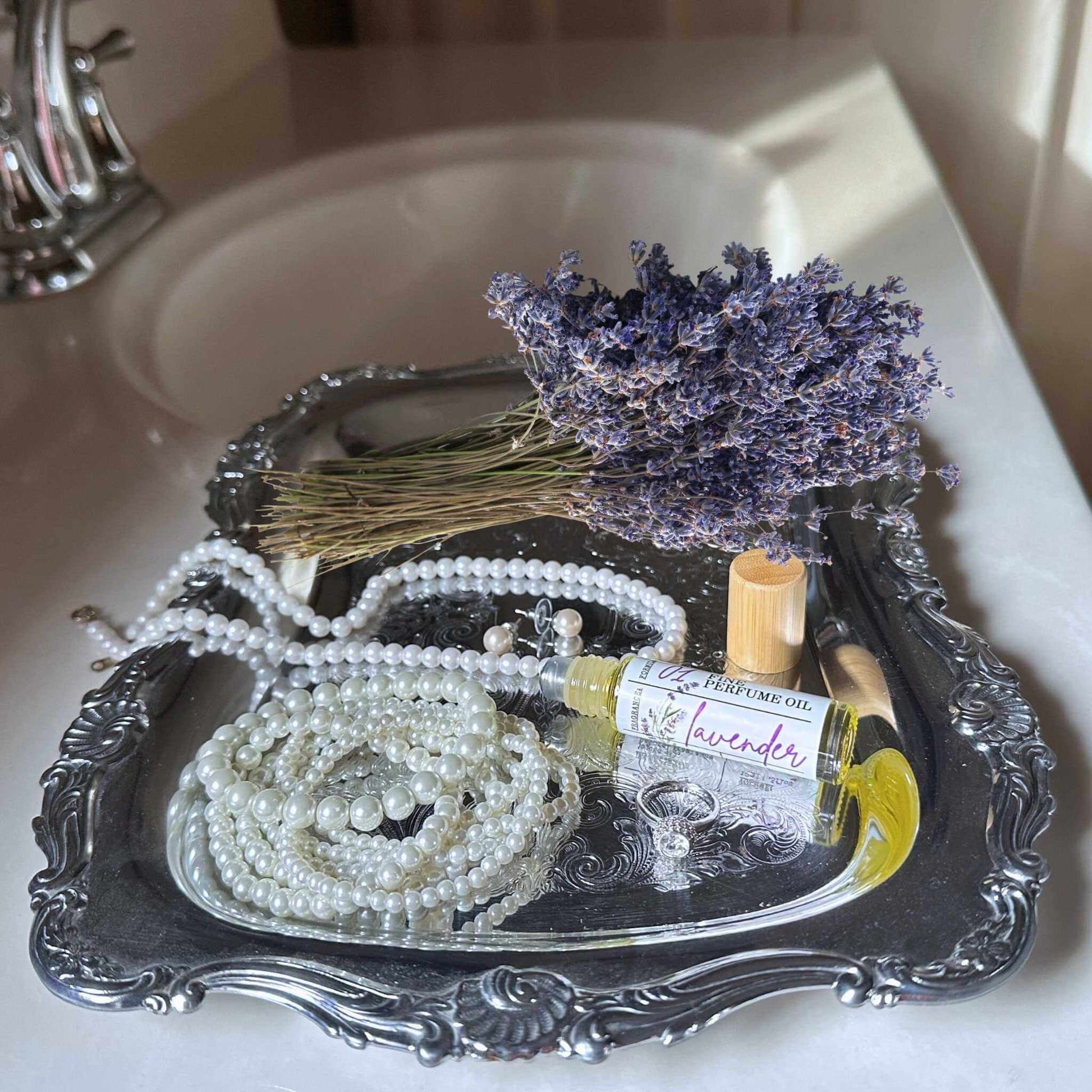 Tray with dried lavender, pearls, and a bottle of lavender perfume on a sink.