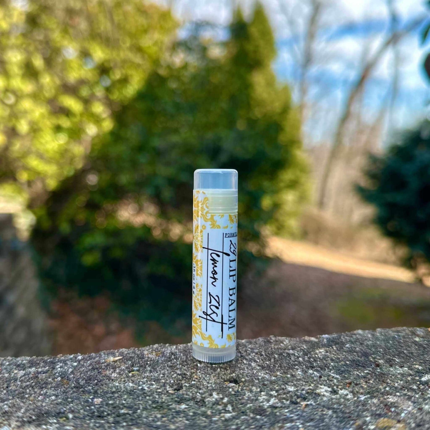 Lip balm tube with lemon zest flavor on a stone surface with a blurred natural background
