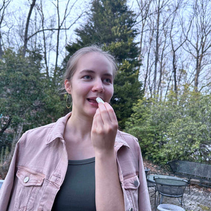 Person applying lip balm outdoors with trees in the background