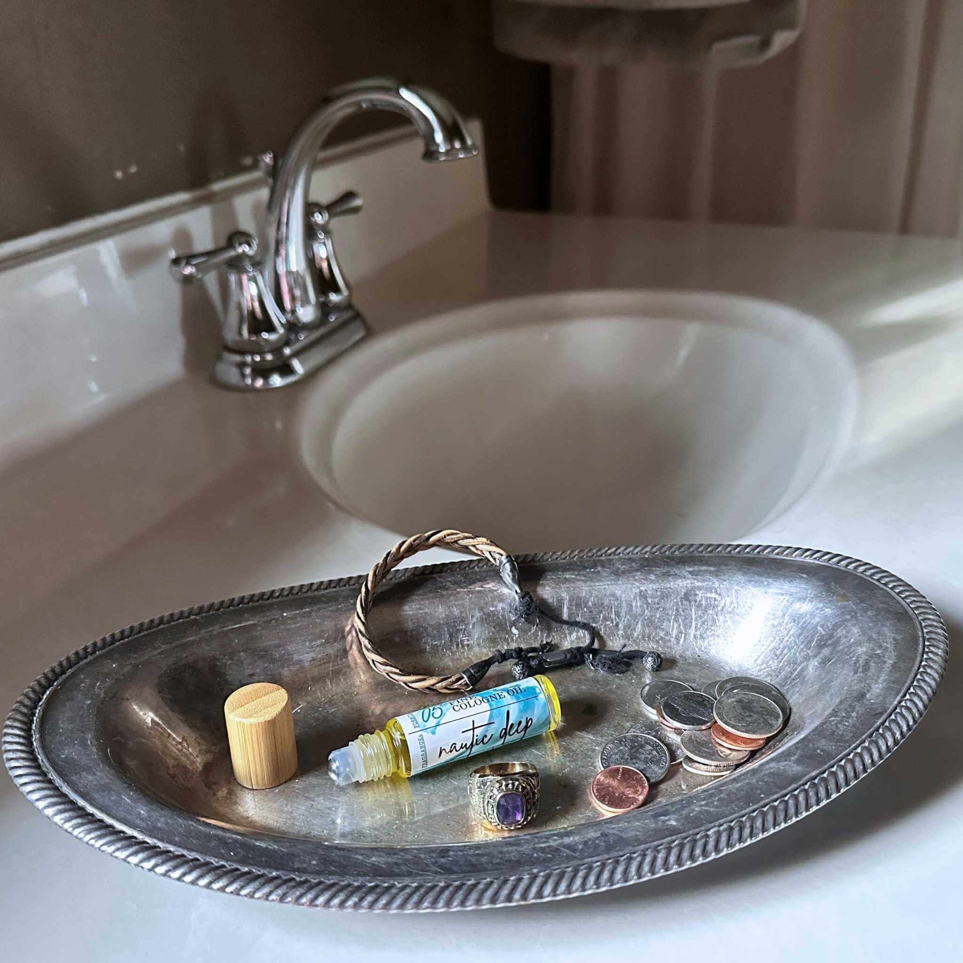 Silver tray with change and a rollon cologne bottle on a bathroom sink