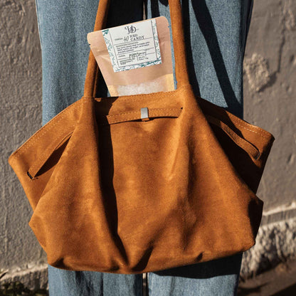 Brown leather bag held by a person with a peppermint candy bag inside, against a neutral background.