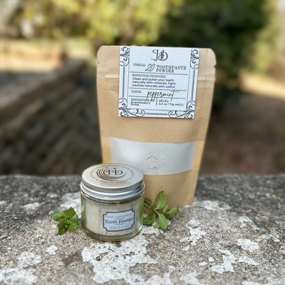 Toothpaste powder jar with a pouch of tooth powder refill on a stone surface.