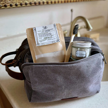 Gray toiletry bag with toothpaste and dental items on a bathroom counter
