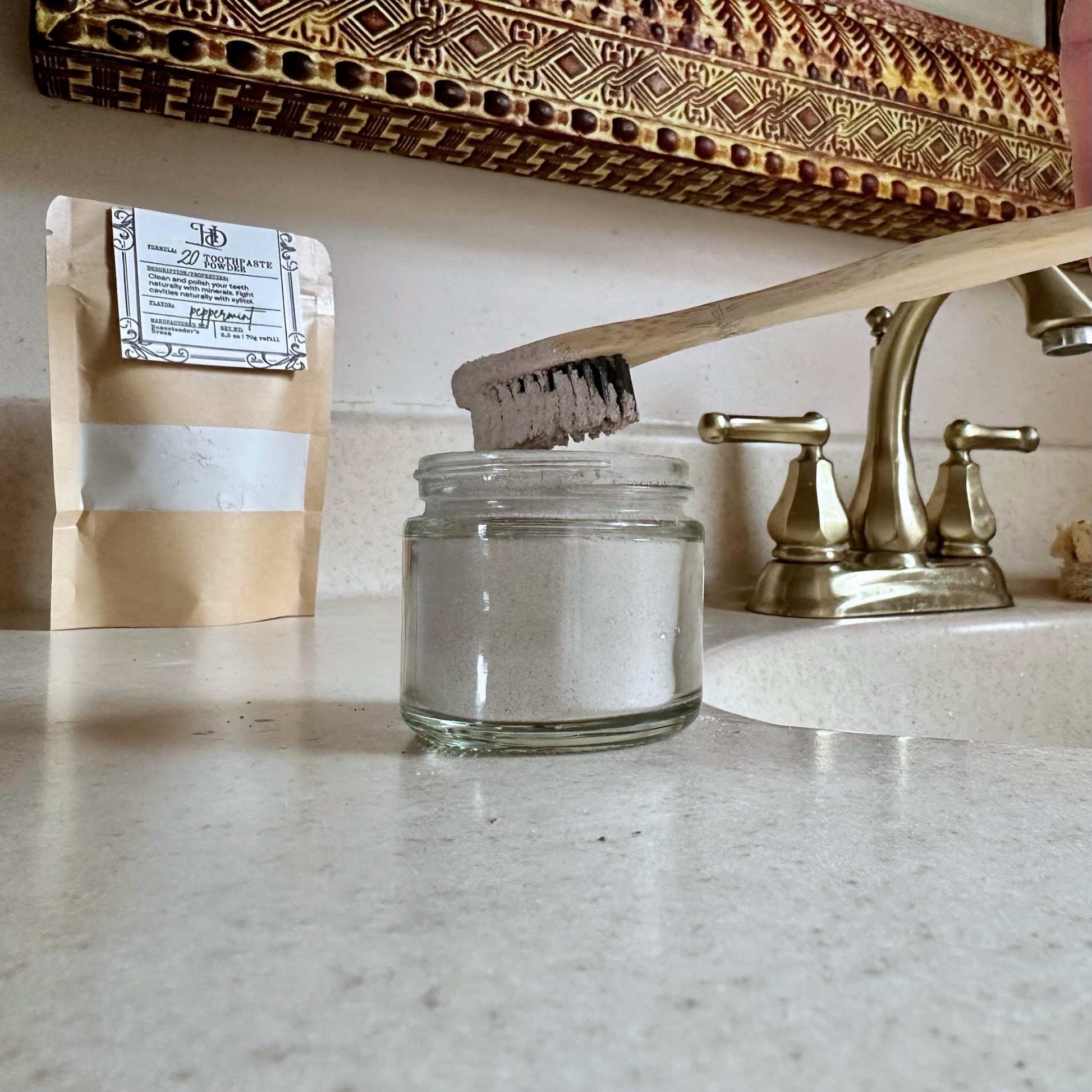 Clear glass jar on a kitchen counter with a wooden scrubber, gold faucet, and brown Kraft bag.