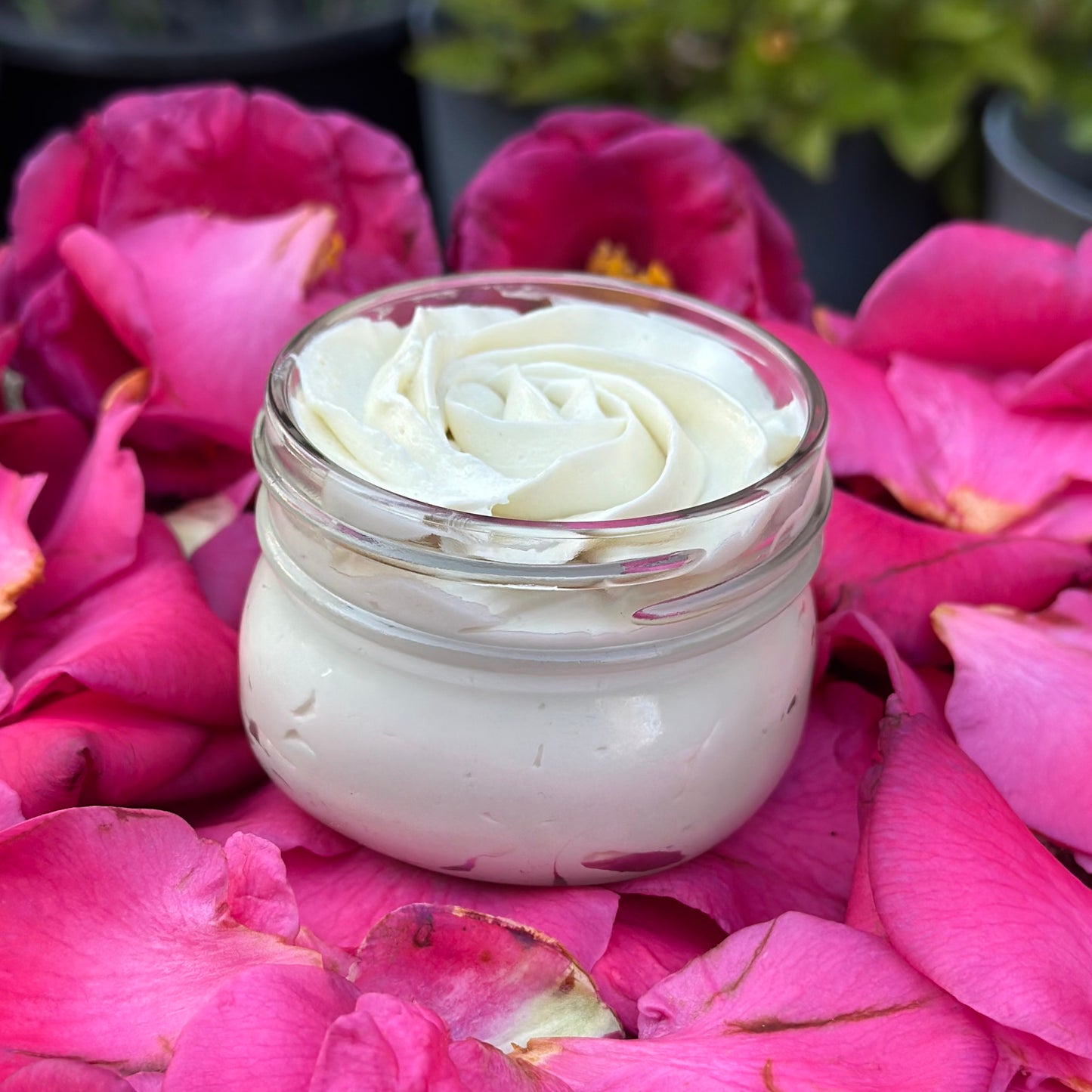 A jar of Romantic Rose Body Butter placed on a bed of pink rose petals, with a soft, moist texture visible outside the jar, revealing the beautiful rose design piped into the jar.